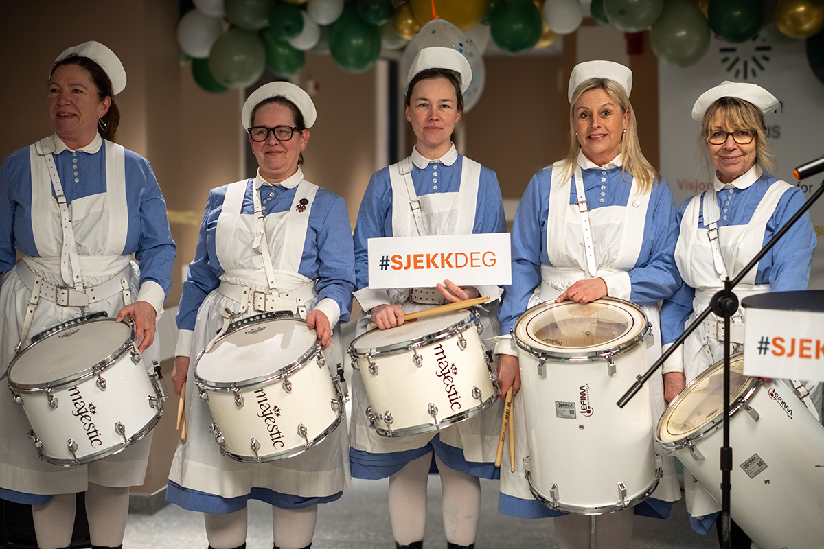 En gruppe sykepleiere iført hvite uniformer og med trommer i hånden